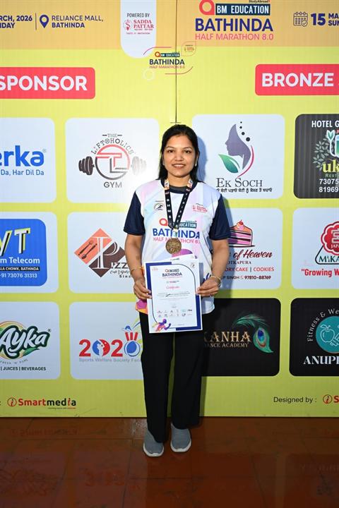 A runner poses with her certificate in front of the Bathinda Half Marathon 8.0 sponsor wall